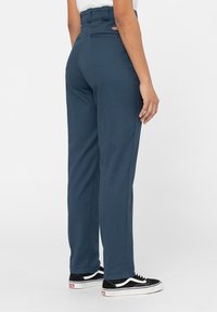 Marinblå högmidjade byxor med skräddarsydd passform, med en bakficka och bältesöglor, kombinerade med svarta sneakers.