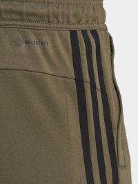 Olive krāsas sporta bikses ar melnām sānu strīpām un AEROREADY logotipu. Izgatavotas no teksturēta auduma, ar elastīgu jostu un kabatas detaļu.
