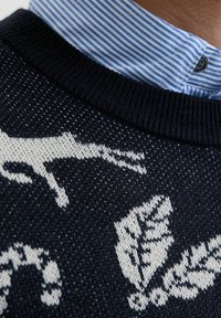 Un pull marin avec des motifs d'animaux et de feuilles blancs, texture tricotée et col rond côtelé. Un col rayé bleu clair est visible en dessous.