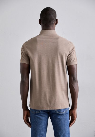 Polo shirt marron à manches courtes, finition texturée et coupe droite, associé à un jean bleu. Vue de l'arrière.
