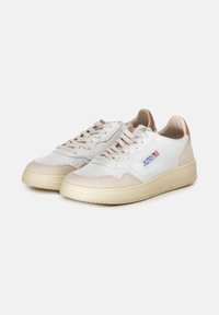Sneakers bianchi con dettagli in suede crema, perforazioni sulla punta e suola in gomma beige. Presentano una piccola etichetta logo sul lato.