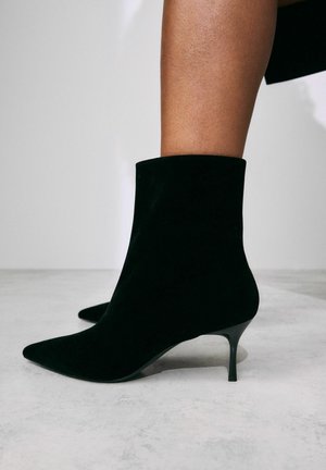 Stivaletti in velluto nero con punta appuntita e tacco stiletto sottile. Il design presenta una vestibilità aderente alla caviglia e una texture liscia.