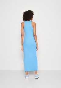 Blue sleeveless maxi dress made of soft fabric, with a fitted silhouette and side slits. Paired with white sneakers featuring blue accents.