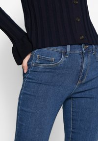 Top azul marino de manga larga con tejido acanalado y botones, combinado con jeans de mezclilla azul que muestran costuras visibles y bolsillos.