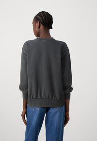 Dark gray sweatshirt with a relaxed fit, ribbed cuffs, and a waistband. Pairing with blue denim, showcasing a casual style.
