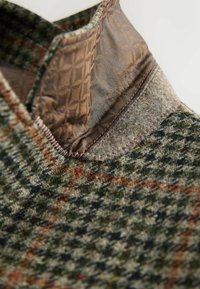 Textureret uldblandingsstof i grønt og brunt hundetand mønster med en blank, brun syntetisk krave og kontraststikning.