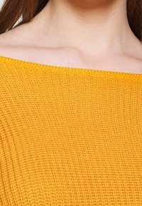 Felgeel, ribgebreide stof met een off-shoulder ontwerp. De textuur is geweven, waardoor het een rekbare en zachte uitstraling krijgt.