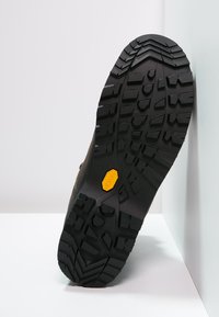 Sola de bota de caminhadas castanha com um padrão de aderência em borracha preta robusta e um proeminente logótipo Vibram amarelo ao centro para uma melhor tração.