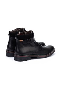 Botas negras de cuero hasta el tobillo con acentos de ante, punta redonda y suela resistente. Presentan cordones en el frente y un cierre lateral. Detalle de costura contrastante.