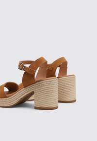 Sandalias de tacón de ante marrón con un amplio tacón de bloque de cuerda trenzada, diseño de punta abierta y tira en el tobillo con detalle de hebilla plateada.
