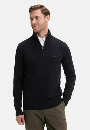 Pull noir à demi-zip en matériau tricoté doux. Il présente un col et des poignets côtelés, avec un petit logo sur la poitrine. Assorti avec un pantalon olive.