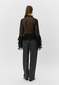 Black sheer blouse with ruffled edges, long sleeves, and a fitted waist, paired with loose gray leopard print trousers.