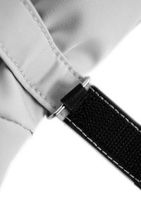 Nahaufnahme eines grauen Stoffes mit einem schwarzen Riemen, der weiße Nähte und ein kleines schwarzes Lederakzent in der Nähe eines Metallrings aufweist.