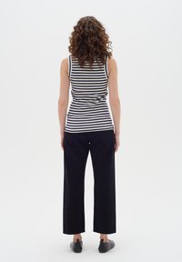 Top senza maniche a righe nere, texture a costine; abbinato a pantaloni neri a vita alta e larghi e scarpe slip-on nere.