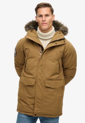 Bruine geïsoleerde parka met een bontgevoerde capuchon, twee voorzakken en een ritssluiting. Getextureerde stof met een gladde afwerking.