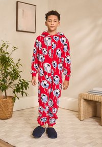 Tutina rossa con cappuccio, caratterizzata da un motivo di palloni da calcio. Realizzata in tessuto morbido, presenta polsini elasticizzati e una cerniera frontale.