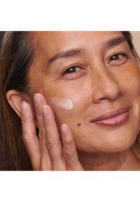 Hydraterende crème aangebracht op een gezicht; de crème is licht en romig, met een zachte textuur. Huidtint lijkt natuurlijk met zichtbare poriën.