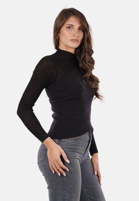Maglione a maniche lunghe a collo alto nero a coste con un design aderente, caratterizzato da un tessuto testurizzato e una finitura liscia. Abbinato a jeans scuri.