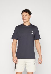 Temno siva majica s kratkimi rokavi z okroglim izrezom, izdelana iz bombaža, s čim manjšo belim Adidasovim logotipom in napisom "Star Wars" na levem prsnem delu.