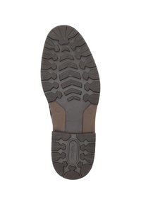 Semelle de chaussure en caoutchouc avec un motif de bande de roulement profond. Comprend des rainures et des formes hexagonales pour une meilleure traction. Logo central présent. Couleur : gris foncé.