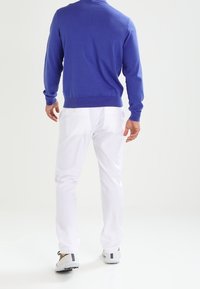 Pull en tricot bleu avec un col rond, associé à un pantalon blanc et des baskets grises. Le pull présente des poignets et une taille côtelés.