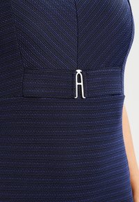 Granatowa sukienka z fakturowanej tkaniny z poziomymi prążkami, podkreślona srebrnym logo na talii.