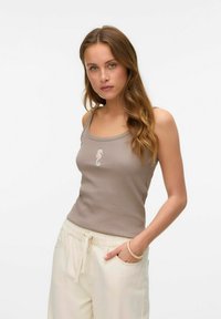 Bruine geribbelde tanktop met een vierkante halslijn en een klein roze paardenhaai borduurwerk, gecombineerd met crèmekleurige broek.