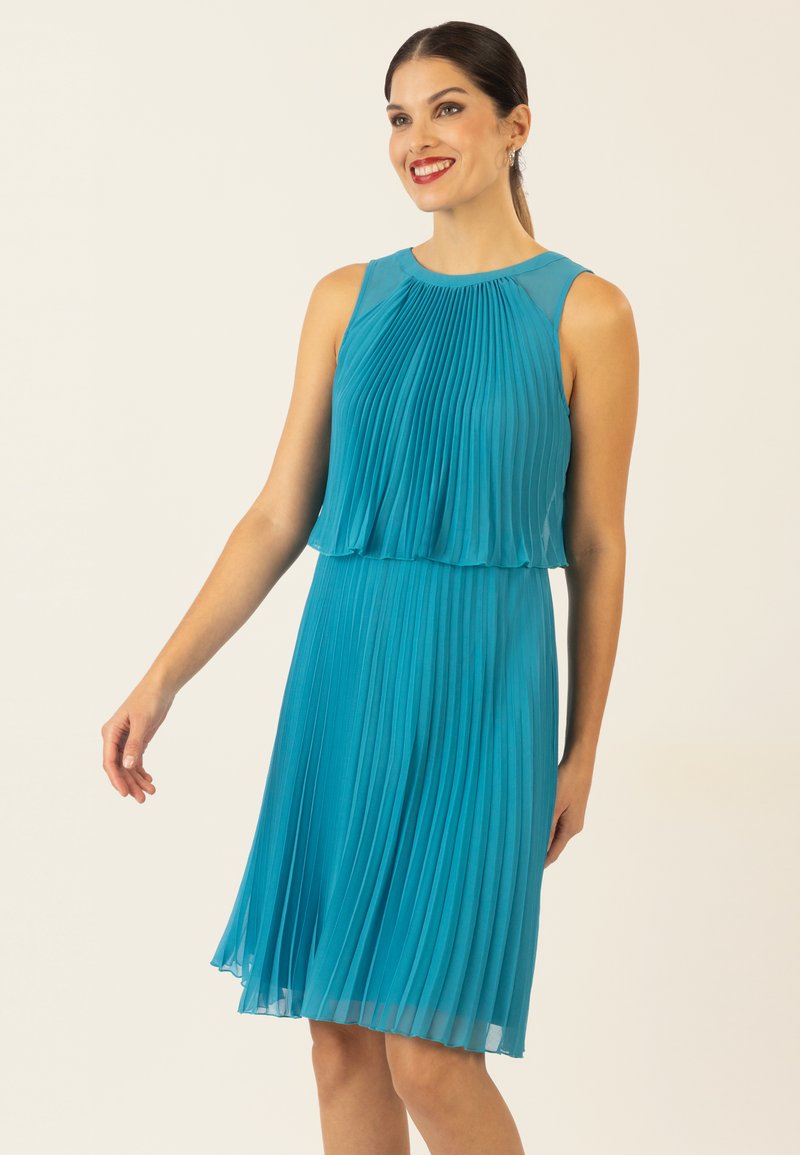 Ein plissiertes teal-farbenes Kleid mit Rundhalsausschnitt, ärmellosem Design und geschichtetem Oberteil, das bis zum Knie fließt und eine leichte Textur hat.
