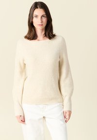 Maglione beige a coste con scollo a barca e maniche lunghe. Realizzato in morbido tessuto testurizzato. Abbinato a pantaloni bianchi.
