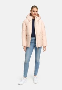 Lichtroze pufferjack met capuchon, voorzien van een rits en zijzakken. Draag het over een marineblauw topje en blauwe denim, in combinatie met witte sneakers.