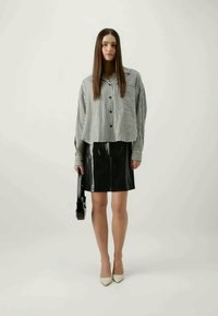 Csíkos fekete-fehér ing zsebbel, fényes fekete latex szoknyával és krémszínű hegyes orrú cipővel párosítva; egy fekete táskát tart.