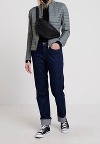 Giacca a vento grigia chiara sopra una maglietta nera, abbinata a jeans blu scuro con risvolti. Borsa a tracolla nera e sneakers nere.