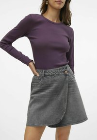 Camisa de manga larga morada combinada con una falda envolvente de mezclilla gris oscuro que cuenta con un cierre de botón y un bolsillo delantero.