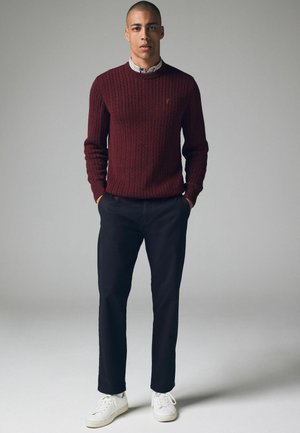 Bordeaux kabelgebreide trui met geribbelde manchetten, gedragen over een geruit shirt, gecombineerd met donkere broek en witte sneakers. Eenvoudig, slim-fit ontwerp.