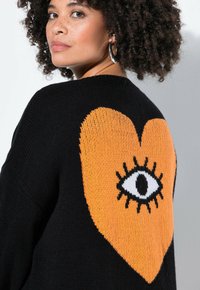 Zwarte trui met een grote oranje hart met een zwart omrand ontwerp van een oog op de achterkant. De gebreide textuur is zacht en comfortabel.