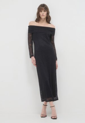 Abito nero off-the-shoulder con lunghe maniche in pizzo, un corpetto aderente e una gonna fluida. Presenta un motivo floreale texturizzato su tutto l'abito.