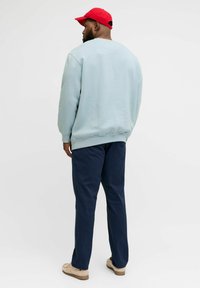 Hanorac bleu deschis cu guler rotund, pantaloni bleumarin și pantofi bej. Șapcă roșie purtată cu viziera în spate. Materialul pare neted, cu o croială lejeră și fără modele.