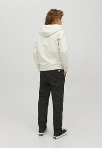 Felpa grigia chiara con finitura testurizzata, abbinata a pantaloni neri. Le scarpe da ginnastica presentano un design in bianco e nero con lacci e dettagli sul tallone.