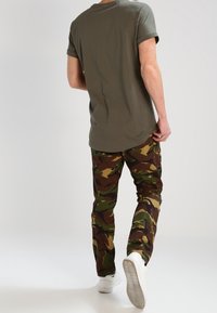 Oliwkowa koszulka z krótkim rękawem połączona z spodniami w kamuflażowy wzór w ziemistych odcieniach. Białe sneakersy dopełniają całość.