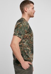 Tričko s krátkým rukávem ve camouflage designu, vyrobené z bavlny, s mramorovaným vzorem v zelené, hnědé a černé barvě, s kulatým výstřihem a volným střihem.