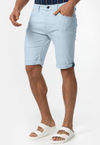 Svijetloplave kratke hlače do koljena od mekog pamuka, s prevrnutim rubovima, prednjim džepom i kopčanjem na dugme. Uparene s bijelim sandalama.