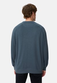 Niebieska bawełniana bluza o luźnym kroju, z raglanowymi rękawami i ściągaczami. Posiada gładką teksturę i delikatne, miękkie wykończenie.