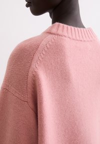 Rosa Strickpullover mit geripptem Ausschnitt und Schulterdetails, der eine weiche Textur und eine lockere Passform bietet.