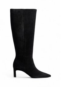 Botte noire en suede montante jusqu'au genou, avec un bout pointu et un talon de hauteur moyenne. Extérieur lisse avec un minimum de détails et une silhouette élégante.