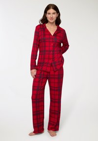 Completo pigiama a quadri rossi e neri con maniche lunghe, camicia con bottoni e pantaloni larghi realizzati in morbido tessuto.