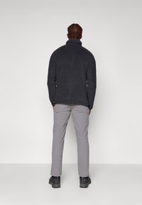 Sudadera de forro polar negra con cuello alto, combinada con pantalones grises claros. La sudadera tiene una textura suave; los pantalones tienen un ligero brillo.