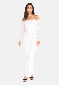Hvid off-the-shoulder blonde top parret med hvide brede bukser. Bukserne har et stofbælte i livet. Sorte hæle sandaler.