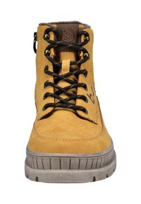 Gelbe Leder-Schnürstiefel mit schwarzen Schnürsenkeln, gepolstertem Kragen, Gummisohle und seitlichem Reißverschluss, frontal auf einem weißen Hintergrund gesehen.