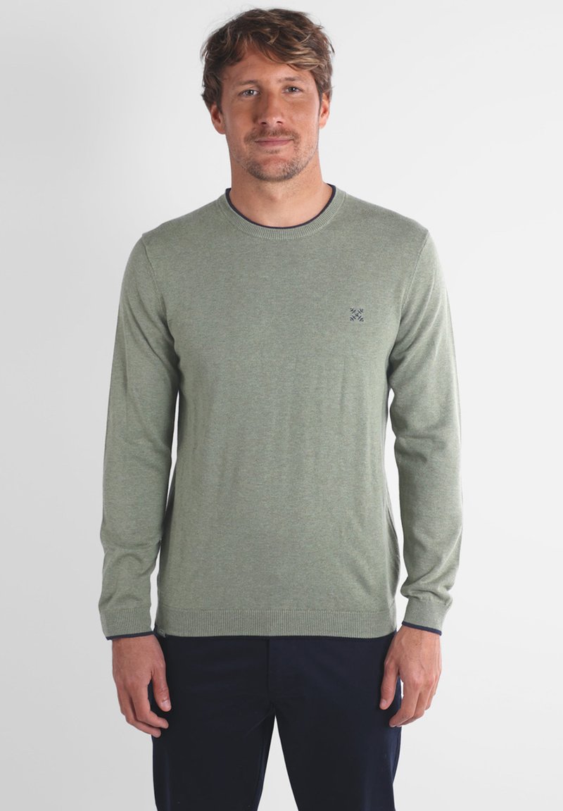 Pull lumineux vert à manches longues, col rond, avec des poignets et un bas côtelés, présentant un petit logo brodé sur la poitrine gauche.