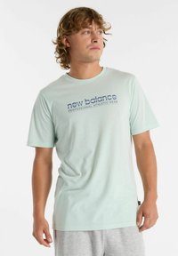 Camiseta de manga corta verde claro hecha de tela suave, con el logo de "new balance" en azul oscuro en el pecho y un cuello redondo.